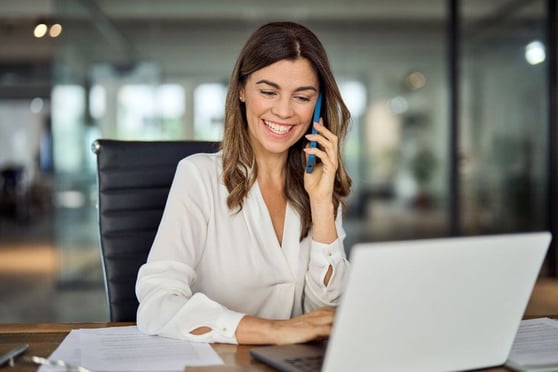 Professional on cellphone at work in office using laptop computer.