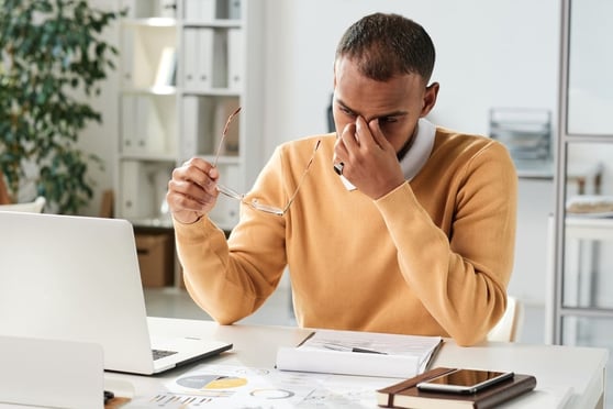 Businessman holding eyeglasses and rubbing bridge of nose while stressed.
