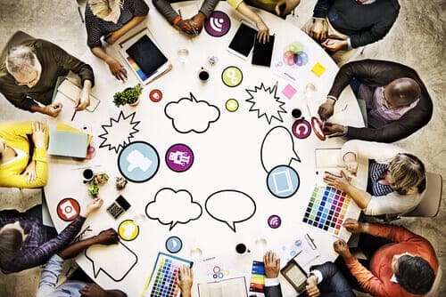 Crane shot of people sitting at a table, with social media icons and laptops visible on the table.