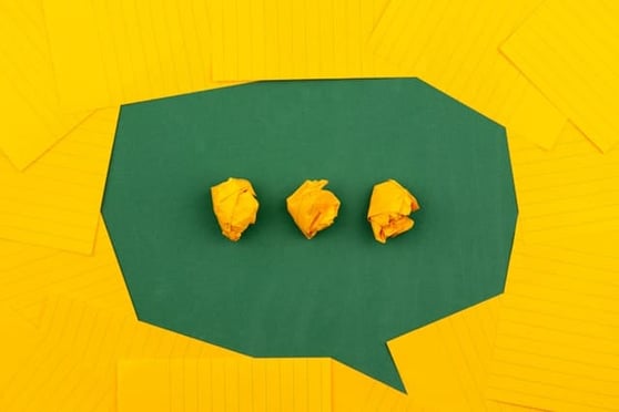 Orange sheets of paper lie on a green school board and form a chat bubble with three crumpled papers.