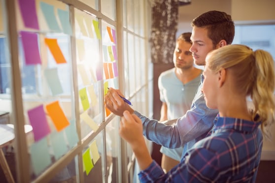People standing in front of a window with colorful sticky notes.