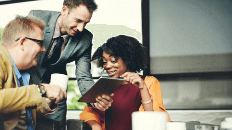 Three people crowding around a tablet, with happy expressions.